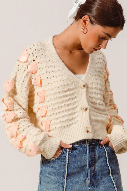 beige holiday cardigan sweater knitwear 
long sleeve button closure v neckline ribbed hem pink bows open knit fabric