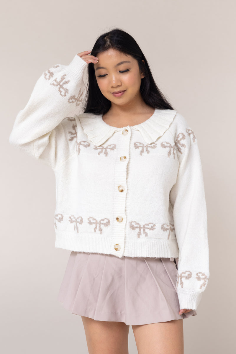 cream cardigan long sleeve button front closure cuffs frill collared round neckline grey bow pattern design