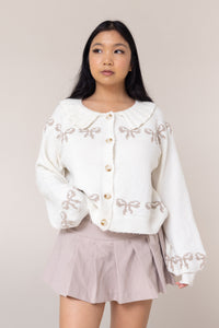 cream cardigan long sleeve button front closure cuffs frill collared round neckline grey bow pattern design